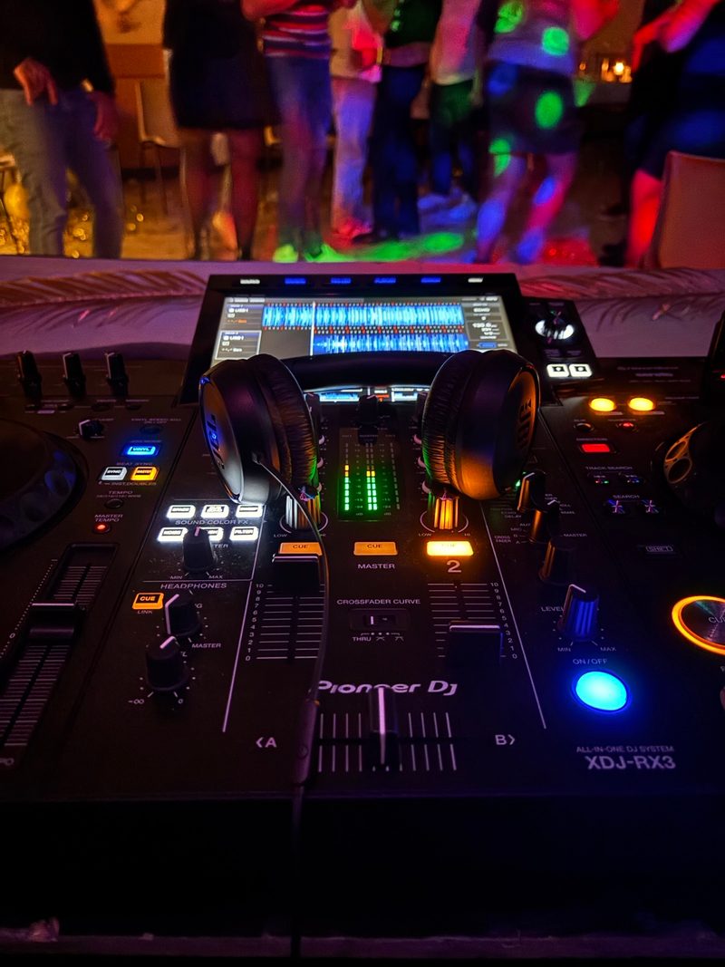 Poste DJ au premier plan, invités qui dansent derrière sous des lumières colorées