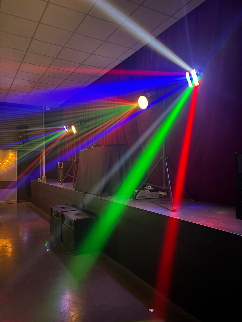 Faisceaux de lumière rouges, verts et bleus qui balaient une salle vide dans la pénombre, devant une petite scène