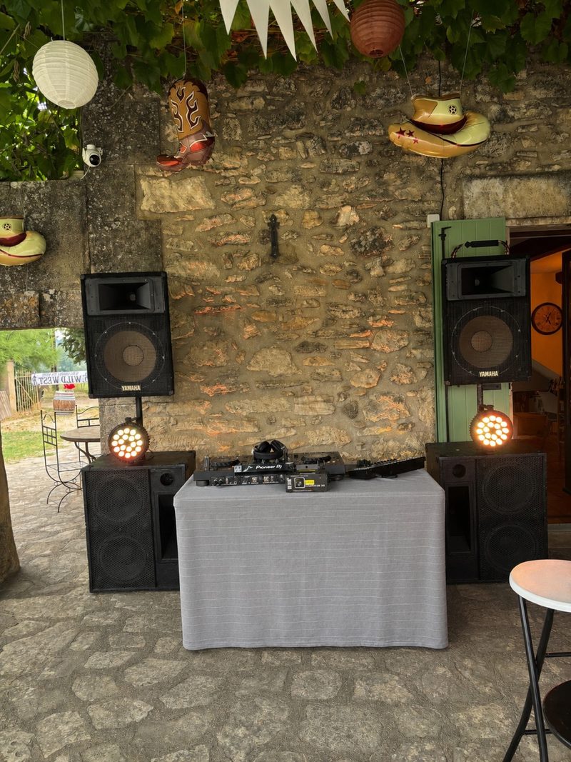 Poste DJ installé devant un mur en pierre décoré de lampions, d'une botte et de chapeaux de cow-boy